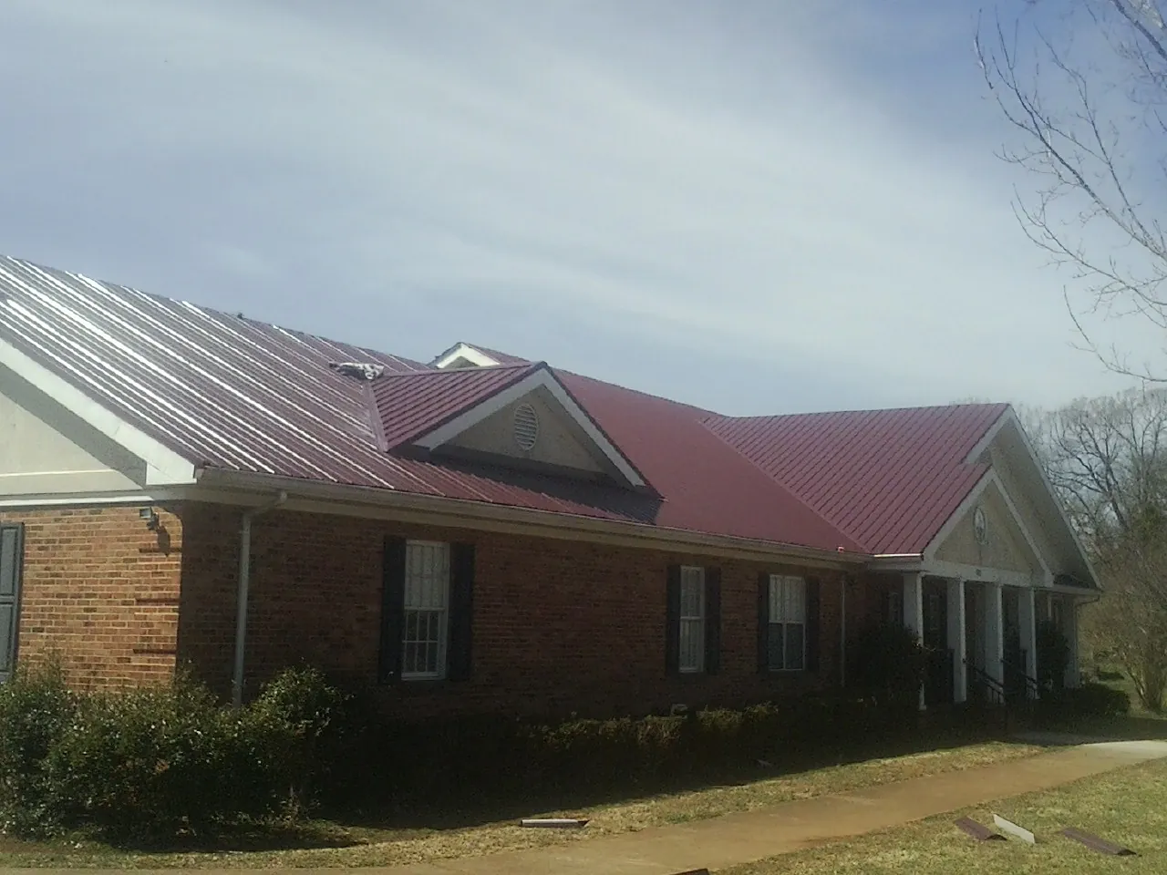 Red metal roof with gabled entries on a long brick building, from a Hail Damage Roof Repair job in Wethersfield