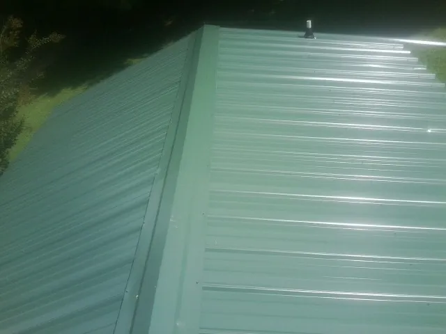 New green metal panels meeting at the ridge of a roof — Flat Roof Repair work by our crew in Wethersfield