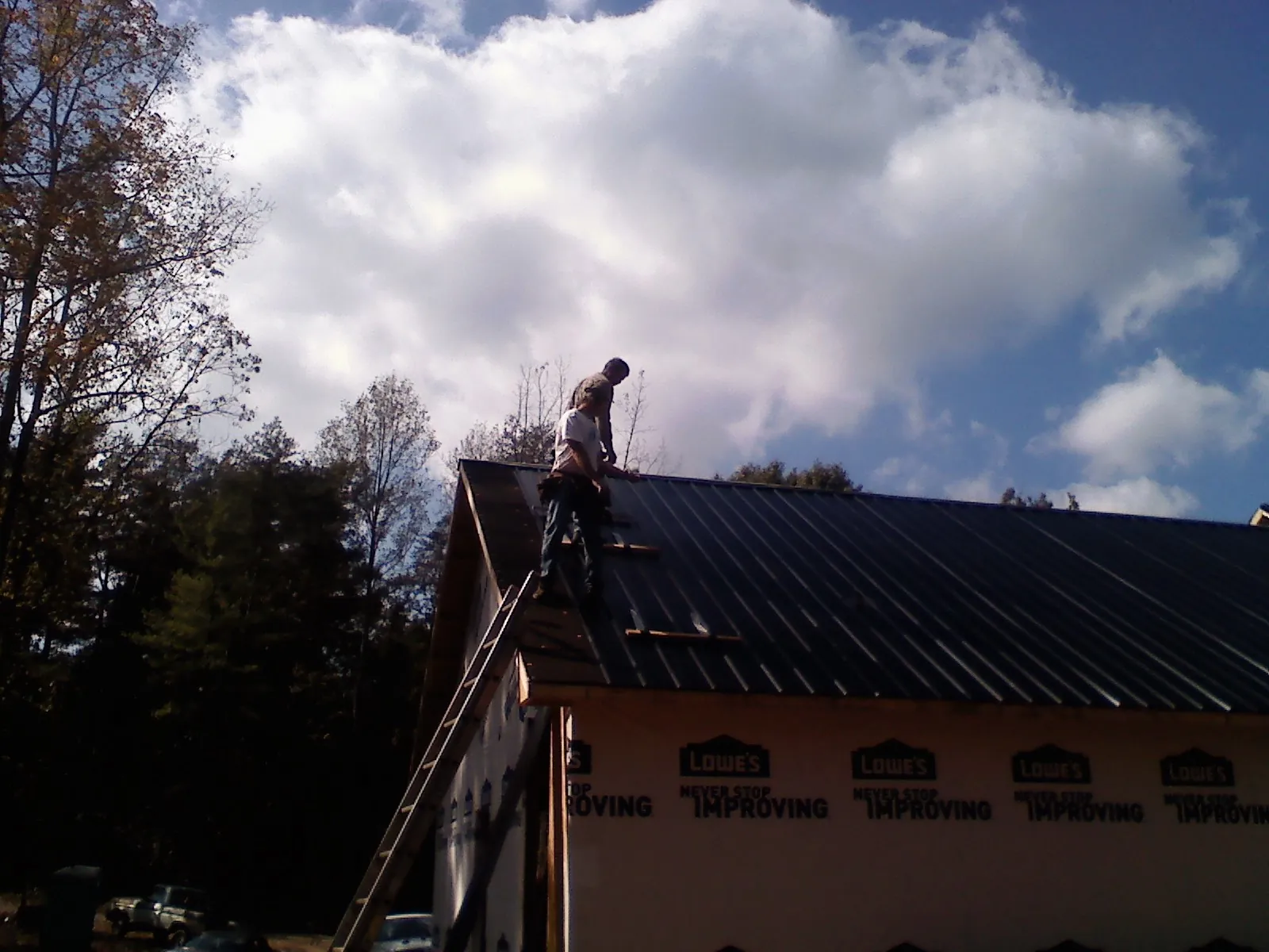 Roofer fastening dark metal panels high against a cloudy sky, from a Roof Inspection job in Wethersfield