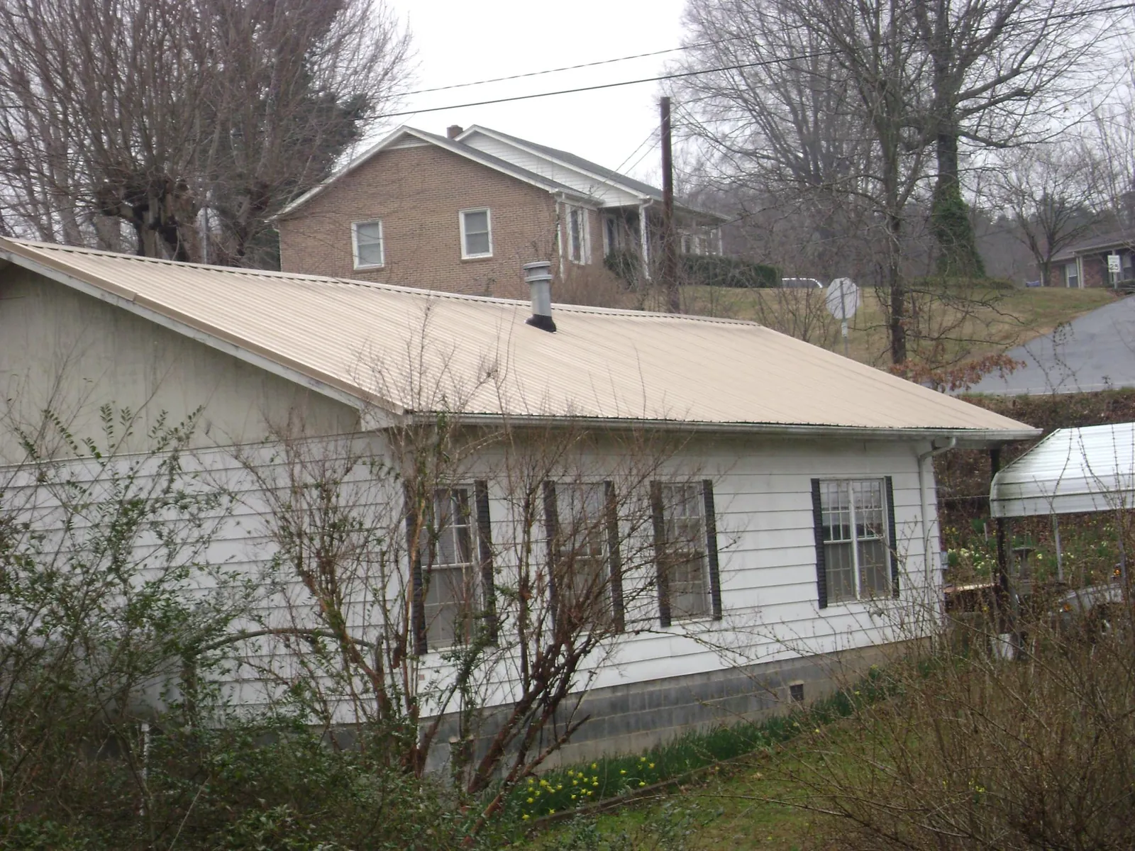 Tan metal roof on a white sided house set into a hillside — Commercial Roofing by Roofing Brothers in Wethersfield